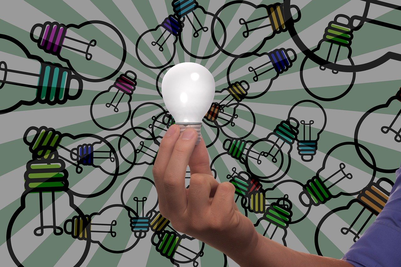 大量の電球が描かれたイラストを背景に、1つの電球を掲げる手